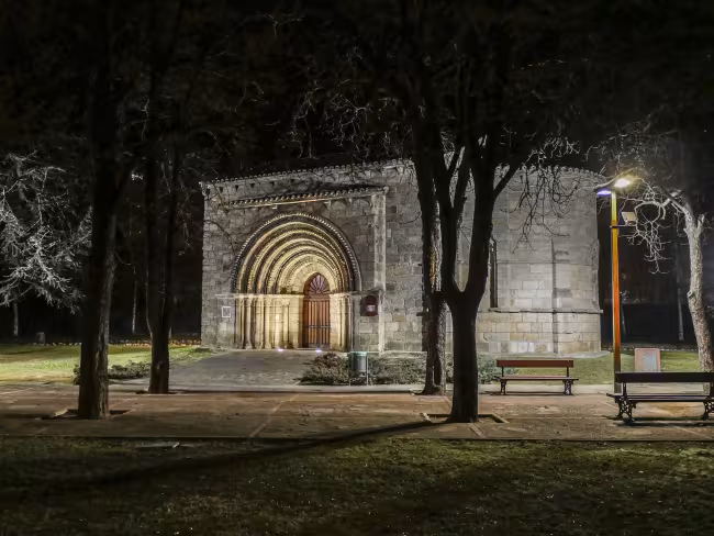 Iglesia románica de San Juan Bautista de noche, con la portada iluminada entre árboles